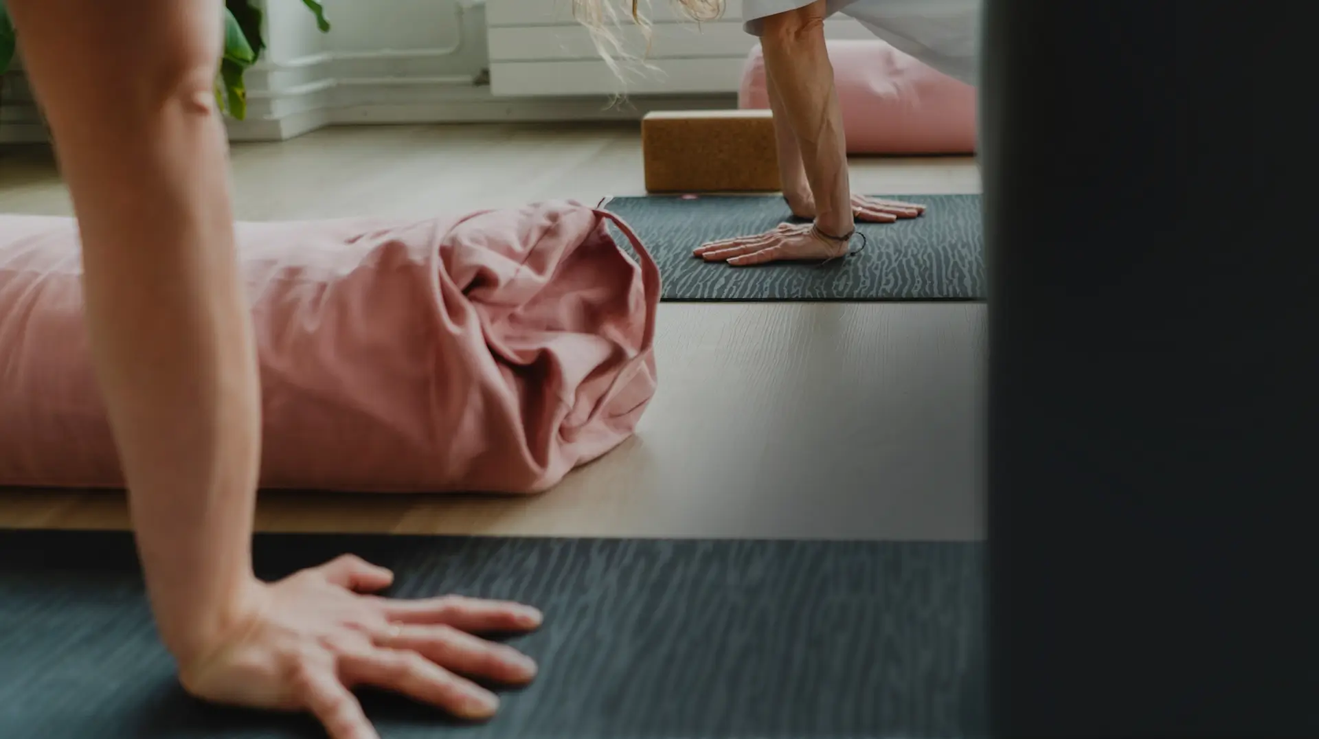 Kädet joogamatolla rauhallisessa joogasalissa, vieressä vaaleanpunainen bolsteri – barajooga helsinki