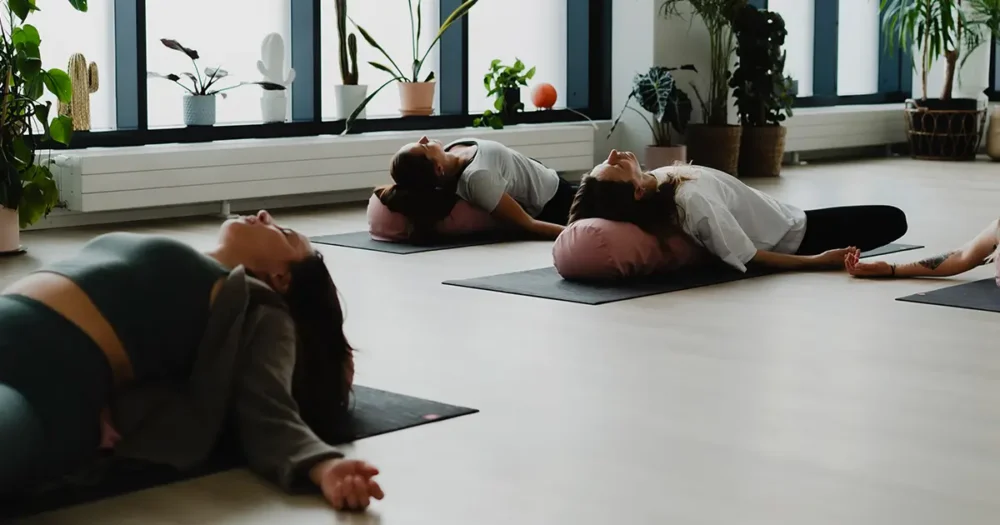 Joogaaja lepää bolsterin päällä hellivä sunnuntai-illan yin -tunnilla, pehmeässä valaistuksessa, jossa keho ja mieli saavat helliä itseään ja rauhoittua viikon lopuksi barajoogan studiossa.