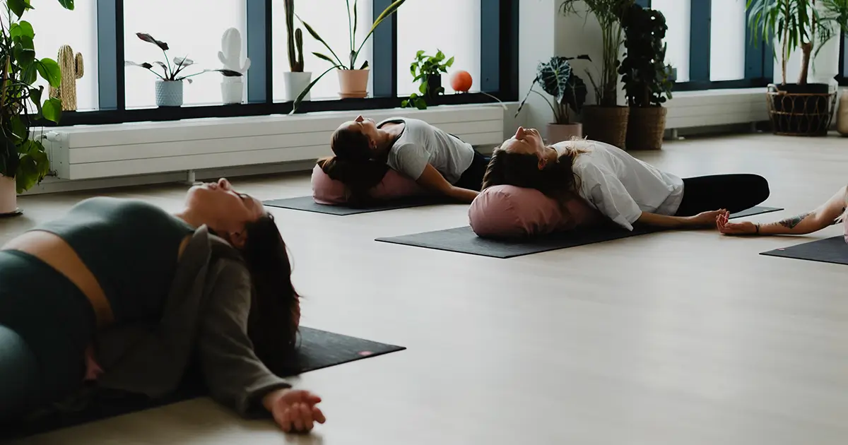 Joogaaja lepää bolsterin päällä hellivä sunnuntai-illan yin -tunnilla, pehmeässä valaistuksessa, jossa keho ja mieli saavat helliä itseään ja rauhoittua viikon lopuksi barajoogan studiossa.