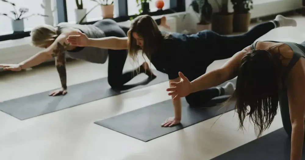 Kolme osallistujaa tekee tasapainoliikettä konttausasennossa käsi ja jalka ojennettuina pilates strong -tunnilla barajoogassa