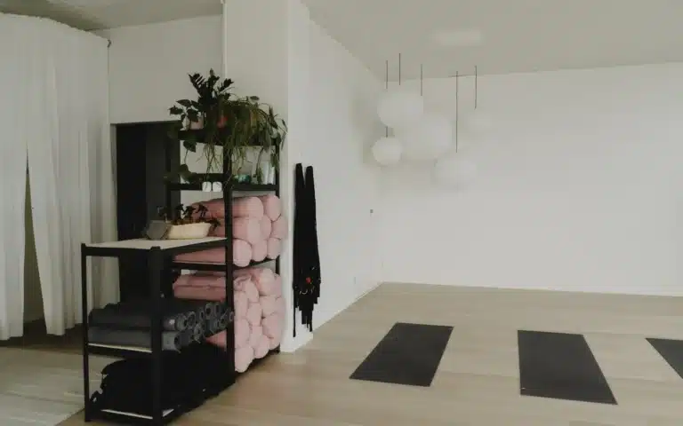 Hylly, jossa vaaleanpunaisia rullattuja mattoja ja tarvikkeita, ja joogamatot lattialla Barajoogan studiolla Sompasaaressa