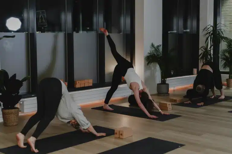 Kolme osallistujaa tekee vinyasa flow -tunnilla alaspäin katsovan koiran asentoa, yksi jalka ilmassa, valoisalla joogasalilla Barajoogan studiossa Sompasaaressa